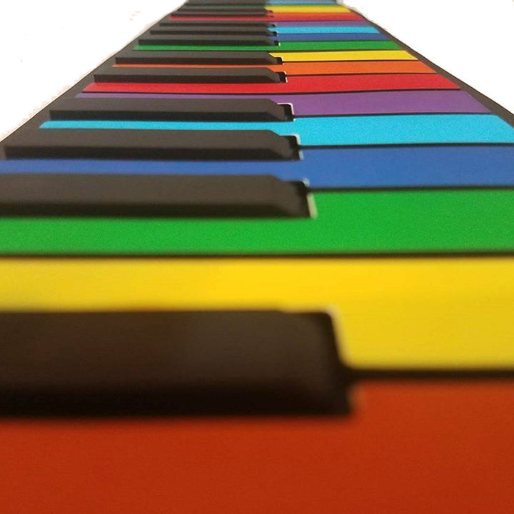 A close-up, angled view of a piano keyboard with brightly colored keys in red, orange, yellow, green, blue, purple, and black, shown against a white background.