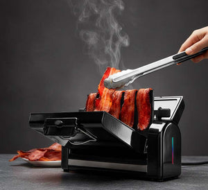 Bacon being cooked on a black bacon toaster with smoke rising, held by tongs.
